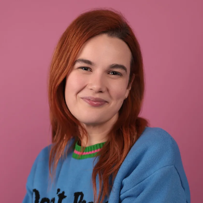 Stephanie Hind, in a blue “Don’t Panic” sweater against a pink backdrop